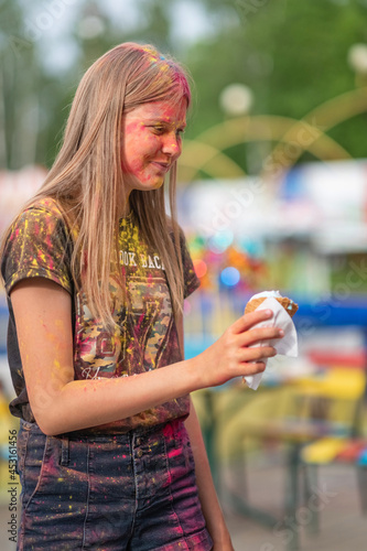 Beautiful girl holly stained with paint in the park eats ice cream.