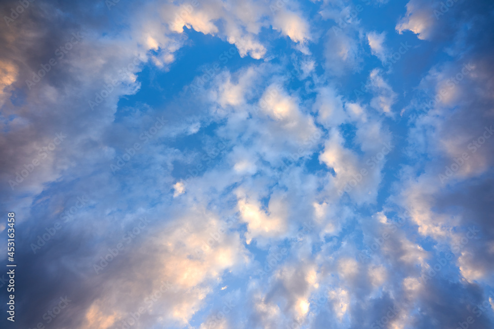 Obraz premium Clouds in front of a blue sky in the morning. Sunlight colors clouds orange. Up view.