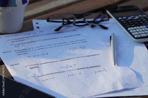 Ejercicios de matemáticas encima de una mesa de madera con un boli, gafas calculadora y teléfono