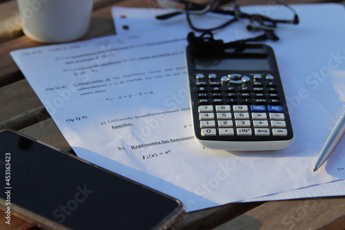 Calculadora encima de papeles con un boli , gafas y móvil al lado. photo