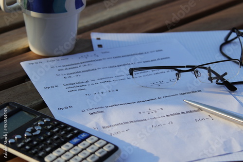Problemas de matemáticas de Bachillerato con un boli y gafas encima y calculadora al lado, encima de una mesa de madera.