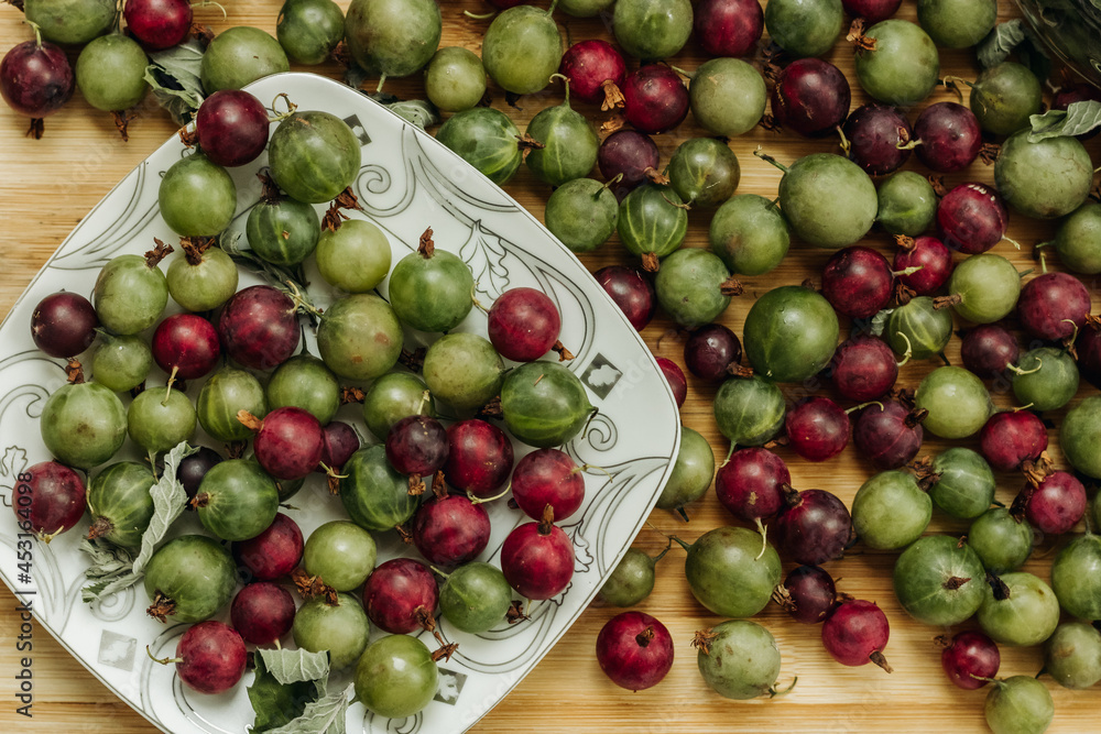 Green and red gooseberries. Gooseberries on a wooden surface and on a white plate. A plate of gooseberries