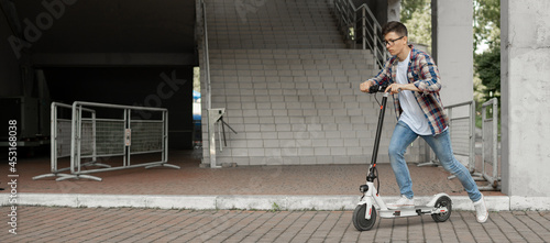A young businessman in a shirt and glasses starts riding an electric scooter. The modern entrepreneur uses modern ecological transport