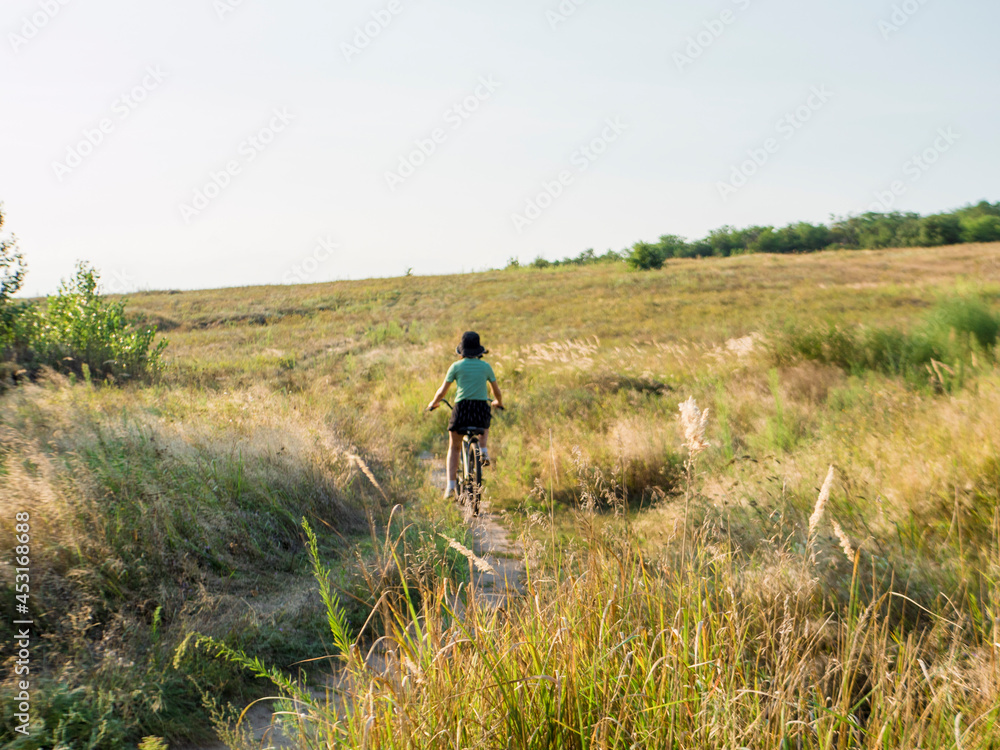 girl in a green t-shirt rides a bicycle in a field at sunset
