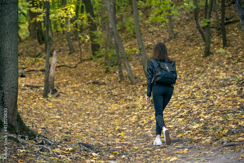 Alone young woman walking in the forest and enjoys autumn. Girl walks through wood, fallen leaves under feet