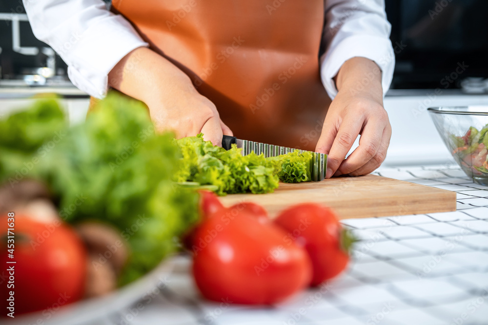 Close up of asian housewife using knife to slice lettuce on wooden chopping board to preparing ingredients Close up of asian housewife using knife to slice lettuce on wooden chopping board to preparing ingredients