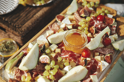 Charcuterie board with maasdam, camembert, brie, cheddar cheese and prosciutto, salami, figs, honey,grapes and cherry tomatoes. Antipasti on wood, mediterranean appetizers on a sunny picnic