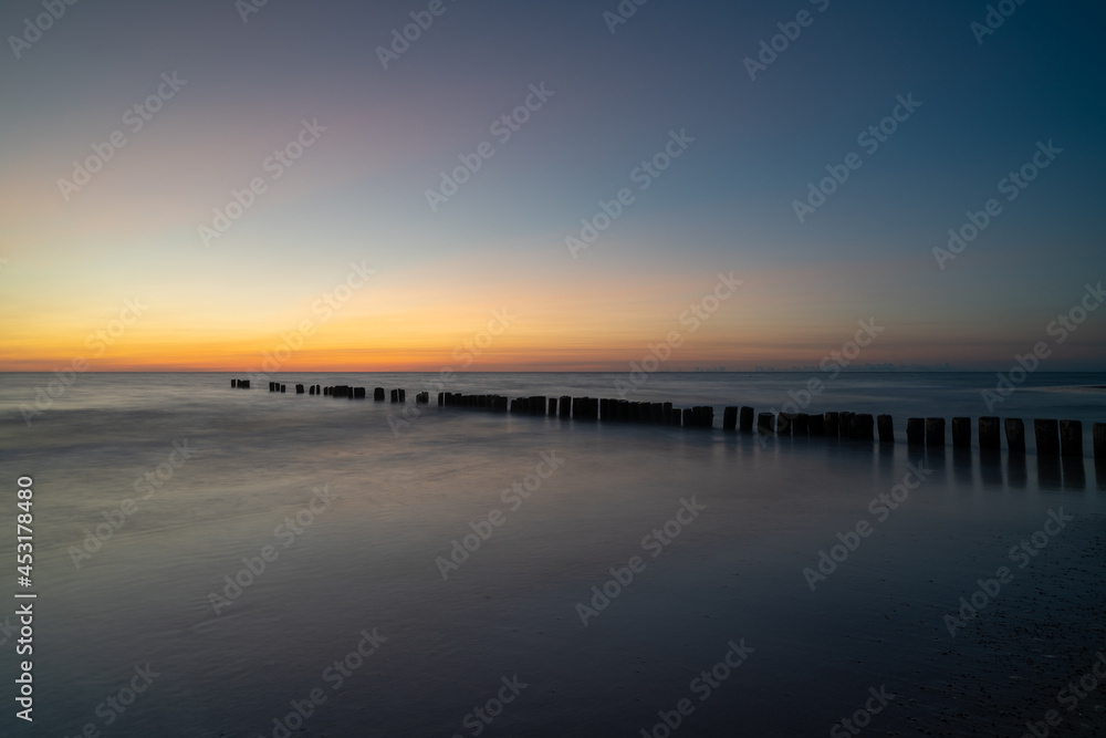 long exposure of an ocean sunset with sandy beach and wooden pylon storm groin in the foreground