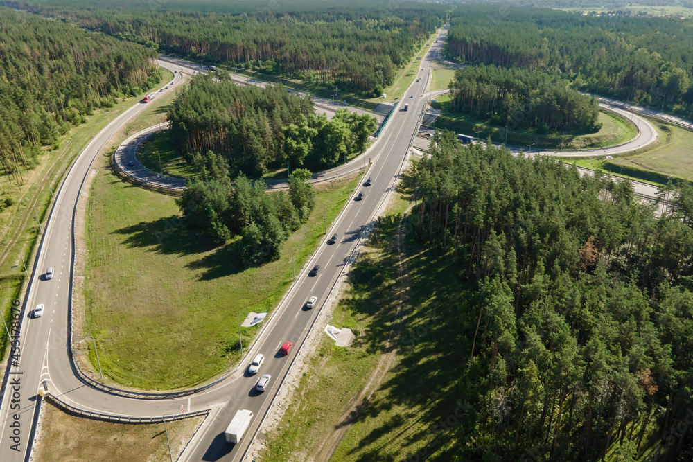 Road junction intersection with car traffic transportation in forest near city, aerial view