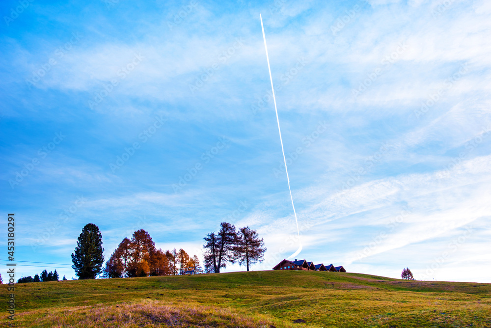 Incredible autumn landscape with row of airplane on the sky above wood houses in Alpe di Siusi in the Dolomites at sunset. The Italian Alps.