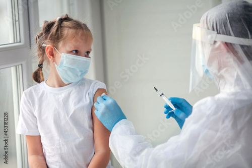 Doctor is hands in rubber gloves makes a shot in the shoulder of a child in a medical mask. Vaccination against coronavirus. COVID-19 vaccine. The doctor vaccinates the child gets a flu shot.