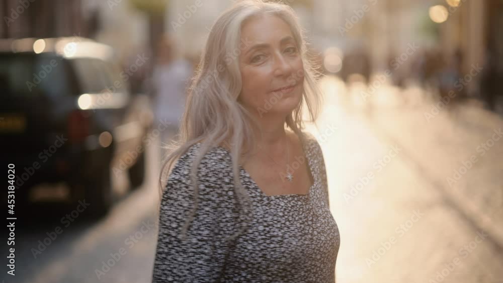 Attractive middle aged senior lady turns around and looks into the camera. Beautiful woman walking down the street. High quality 4k footage