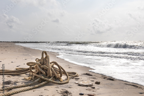 a marine rope washed up on the shore of Jutland, Denmark by the sea. Endless and lonesome sandy beach with beautiful surf in the background