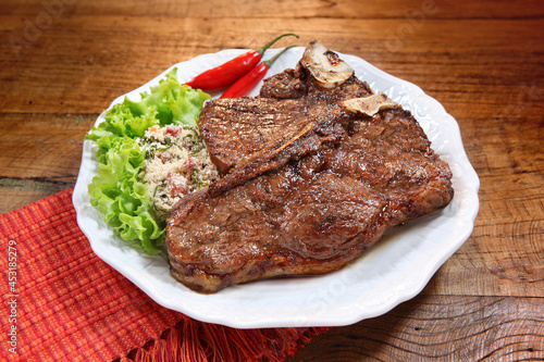 Filé T-bone grelhado com salada no prato em fundo de mesa rústica.