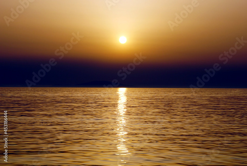 An apocalyptic black cloud above the gold color surface of the wavy sea at sunset