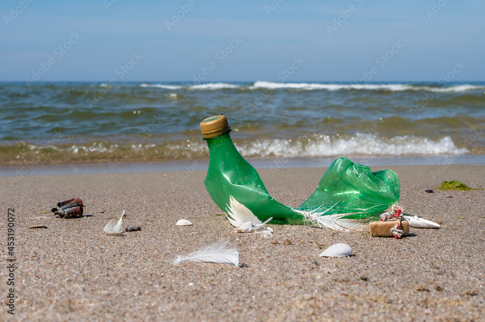 Obraz premium Garbage on the beach. Plastic on the beach. Pollution of the coast with plastic bottles. Green empty bottle.