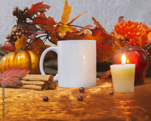 Mug Mock up of one 11 oz white glossy coffee mug on autumn and thanksgiving themed decoration with pumpkin, orange autumn plants, candle, and apple.