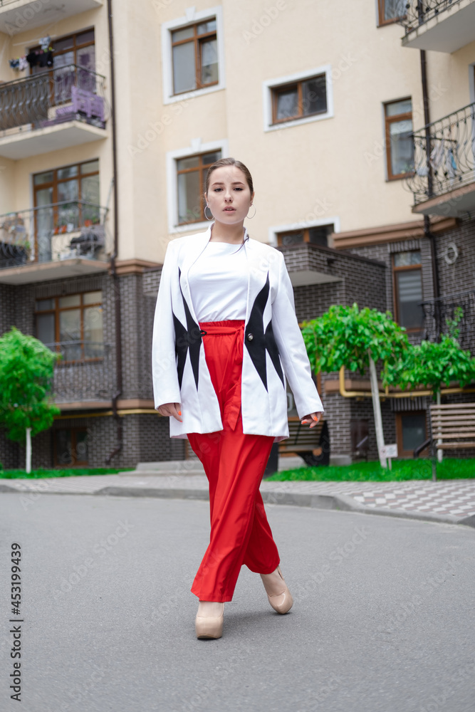 business woman in red pants, white blouse and jacket walking by the street