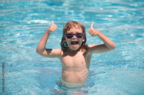 Child in summer swimming pool. Cute child boy with thumbs up swim in swimming pool, summer water background with copy space. Funny kids face. Thumbs up.