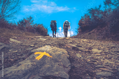 Two Pilgrims Hiking up a Hill with the Yellow Arrow Way Mark outside Sarria along the Way of St James Pilgrimage Trail Camino de Santiago photo