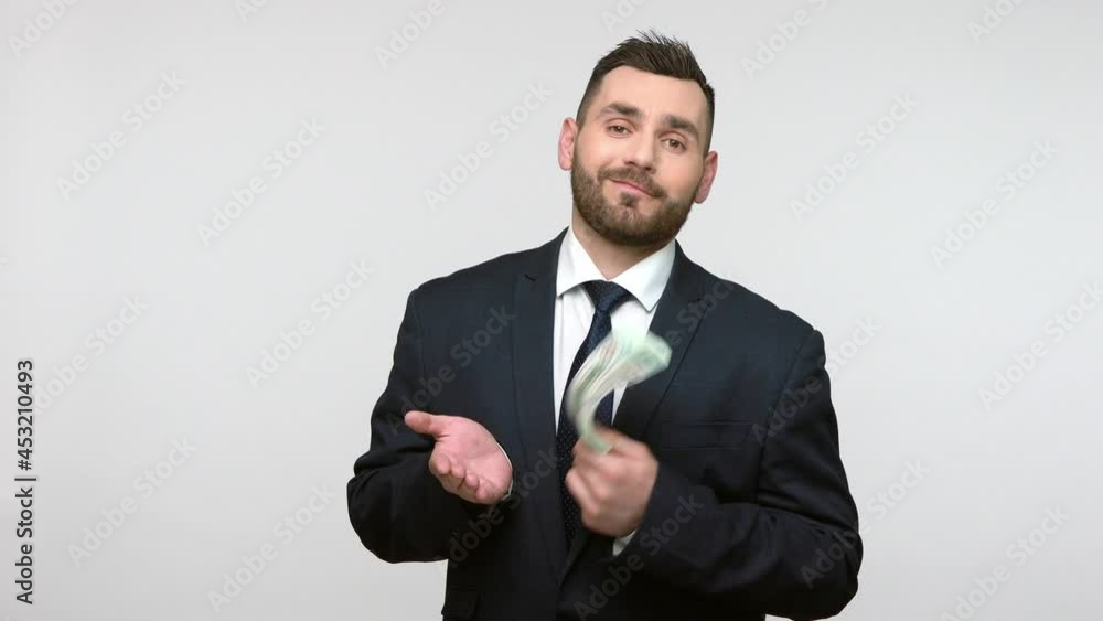 Portrait of satisfied bearded businessman in black official style suit standing with dollars banknotes, looking at camera with proud expression. Indoor studio shot isolated on gray background. Portrait of satisfied bearded businessman in black official style suit standing with dollars banknotes, looking at camera with proud expression. Indoor studio shot isolated on gray background.