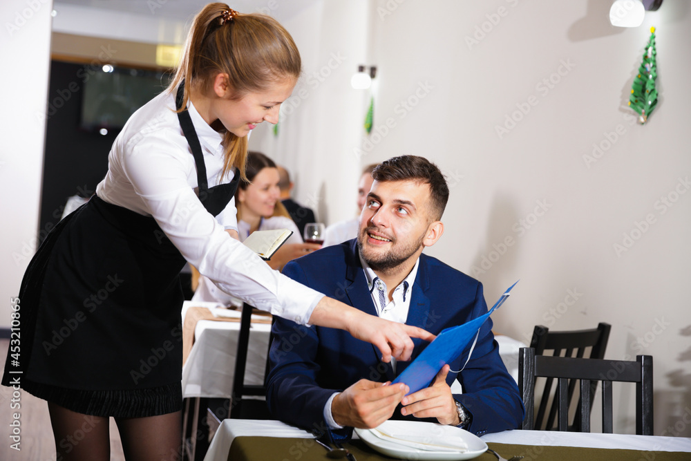 Fototapeta premium Welcoming female waiter is taking order from businessman in restaurante indoor.