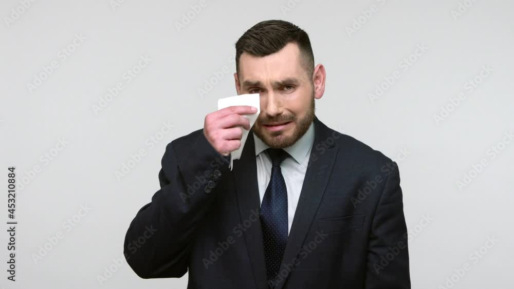 Depressed bearded businessman in black official style suit crying hard, suffering depression, middle age crisis, wipe tears with handkerchief. Indoor studio shot isolated on gray background. Depressed bearded businessman in black official style suit crying hard, suffering depression, middle age crisis, wipe tears with handkerchief. Indoor studio shot isolated on gray background.