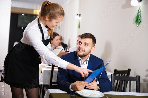 Welcoming female waiter is taking order from businessman in restaurante indoor.