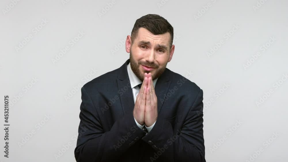 Please, I beg you! Hopefull bearded businessman in black official style suit praying for help, expressing big hope with imploring pleading eyes. Indoor studio shot isolated on gray background.