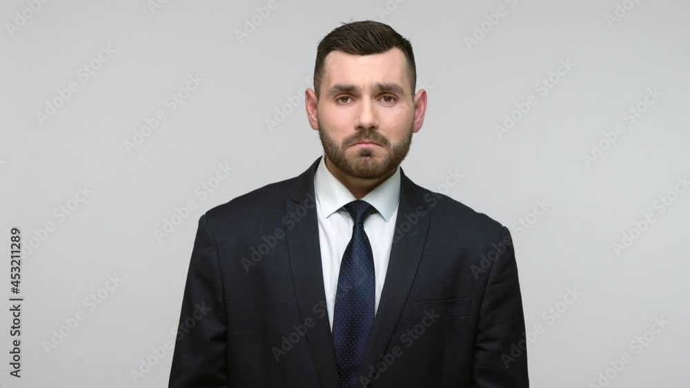Sad bearded businessman in black official style suit having problems at work, feels sadness, looking at camera with upset expression. Indoor studio shot isolated on gray background. Sad bearded businessman in black official style suit having problems at work, feels sadness, looking at camera with upset expression. Indoor studio shot isolated on gray background.