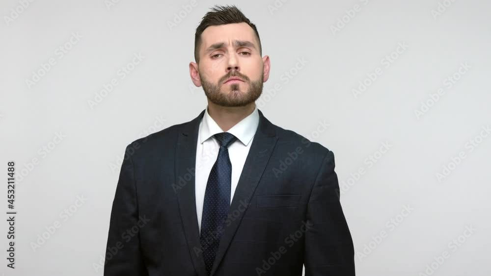 Bearded young adult businessman in official style suit holding hand near head giving salute and listening order with responsible expression. Indoor studio shot isolated on gray background. Bearded young adult businessman in official style suit holding hand near head giving salute and listening order with responsible expression. Indoor studio shot isolated on gray background.