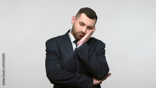 Lazy bored sleepy man in suit standing leaning on hand, looking at camera with bored indifferent expression, exhausted of tedious communication. Indoor studio shot isolated on gray background. photo