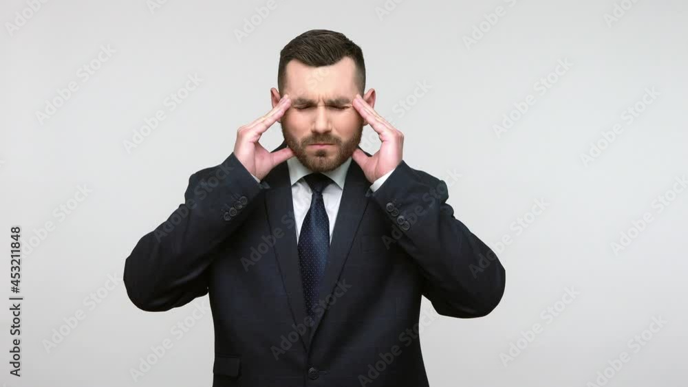 Portrait of unhealthy depressed bearded businessman in black official style suit suffering migraine, high blood pressure, having terrible headache. Indoor studio shot isolated on gray background. Portrait of unhealthy depressed bearded businessman in black official style suit suffering migraine, high blood pressure, having terrible headache. Indoor studio shot isolated on gray background.