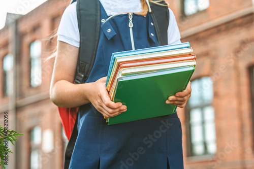 Close-up, A child of an elementary school student holds books in her hands and goes back to school. First day of study. Against the background of the old college. Concept on the topic of education.