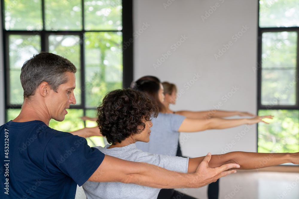 Group of Healthy Asian woman do yoga practicing and body stretching exercise together with male instructor in yoga studio. Female friends enjoy indoor activity lifestyle and sport training workout.