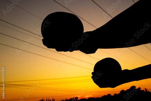 Silhouette photo of a person holding two round objects in the air at sunrise. Conceptual image for getting ready, beginning, resistance training, juggling, and competency.