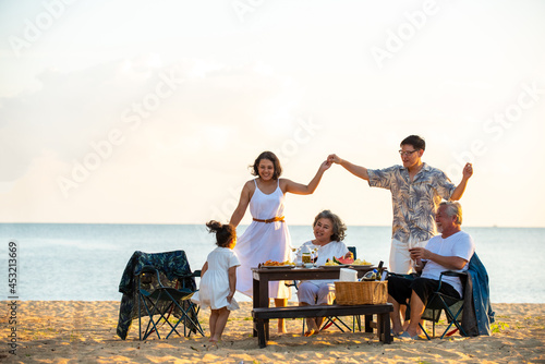 Happy Asian family on holiday vacation. Group of multi generation family little girl with parents and grandparents relax and enjoy with dinner party and dancing together on the beach at summer sunset. © CandyRetriever 