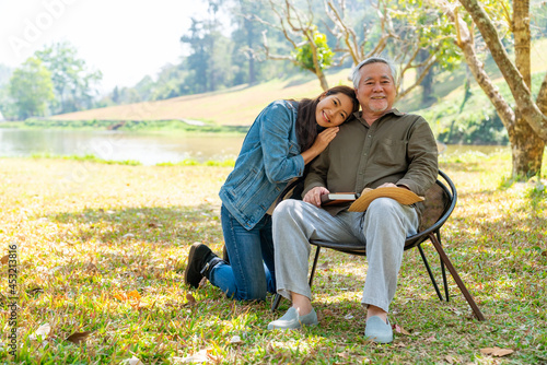 Asian woman caring and hugging senior man grandfather sitting on outdoor chair in the park. Elderly retired male relax and enjoy outdoor activity together with daughter. Family relationship concept © CandyRetriever 