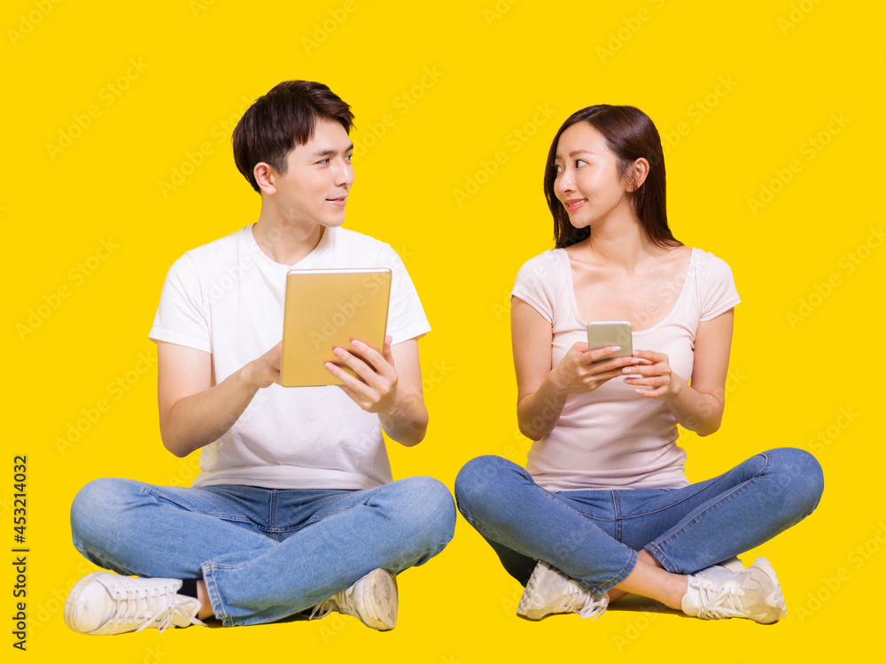 Young man and woman using tablet computer and smartphone.Isolated on yellow background. Young man and woman using tablet computer and smartphone.Isolated on yellow background.