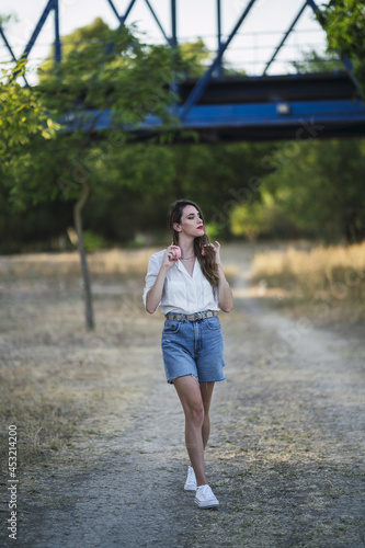 Young Spanish woman with headphoneswearing shorts with a white shirt and walking in a park photo