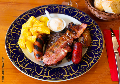 Grilled sausages and pork with potatoes and sauce at plate