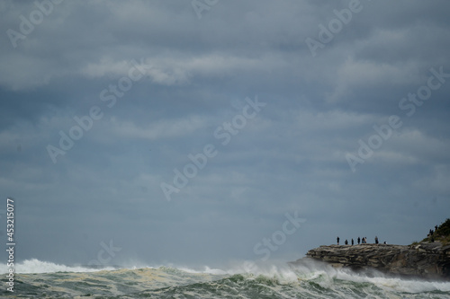 people standing on a cliff looking at the storm over the sea