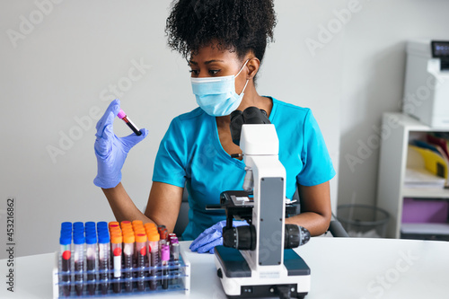 Black medical professional in a mask looks at blood sample label photo