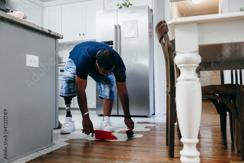 African American man doing chores around the house, sweeping, disabled photo
