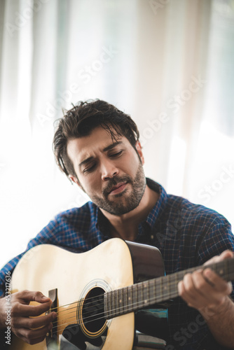 Foto Handsome young man relaxing and enjoying playing guitar with eyes closed at home