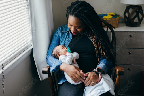 Black mom rocking baby in nursery chair