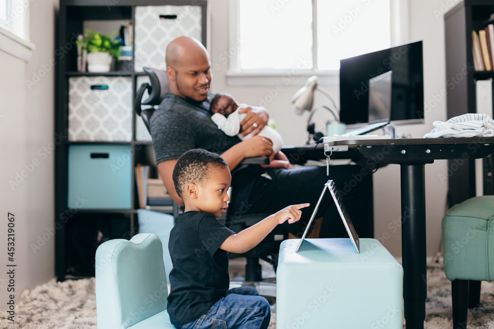 © Creative Flame - Black dad with newborn working from home helping son with schoolwork