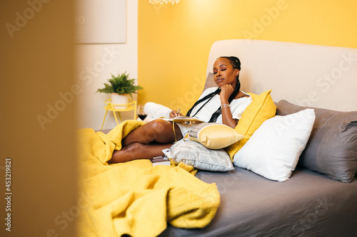 Black woman writes in journal at home in bed photo