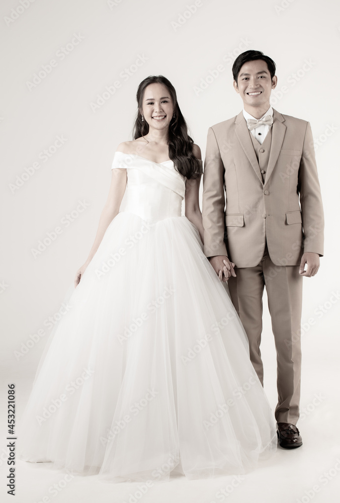 Full length of young attractive Asian couple, man wearing beige suit, woman wearing white wedding gown standing together holding hands. Concept for pre wedding photography