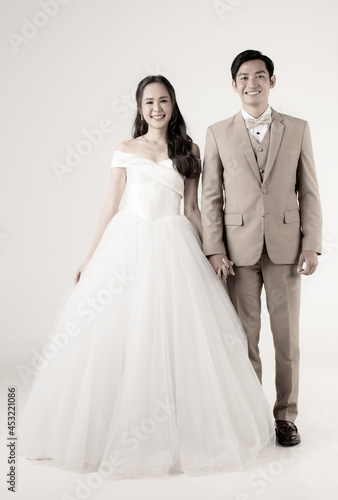 Full length of young attractive Asian couple, man wearing beige suit, woman wearing white wedding gown standing together holding hands. Concept for pre wedding photography